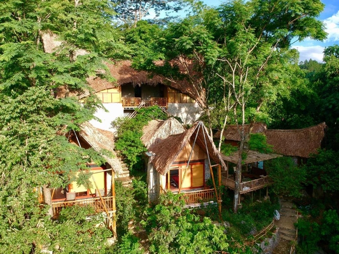 Những căn nhà mái lá cọ ẩn hiện dưới tán cây xanh trong khu nghỉ Moc Chau Retreat. Ảnh: Booking